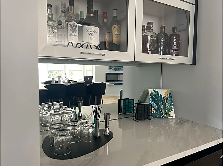Custom home bar area at a Lake Macatawa residence featuring glass-front liquor cabinets, glassware, a quartz countertop, and modern finishes.