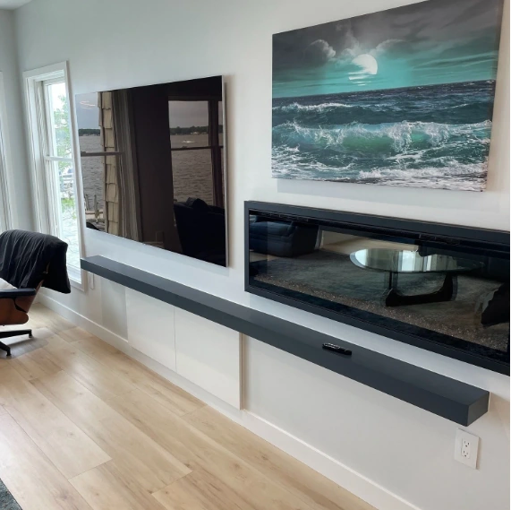 Lake Macatawa living room media wall with a wall-mounted TV, modern linear fireplace, floating shelf, and contemporary coastal artwork.