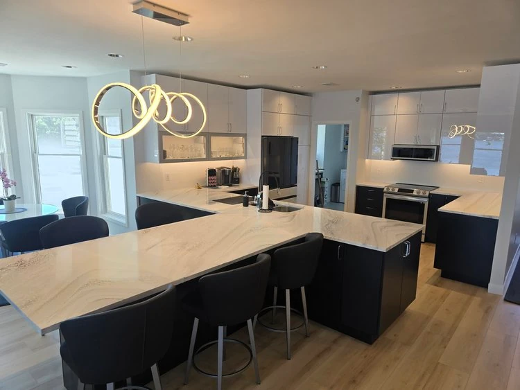 Modern Lake Macatawa kitchen remodel featuring a large island, black lower cabinets, white upper cabinetry, contemporary lighting, and light wood flooring.