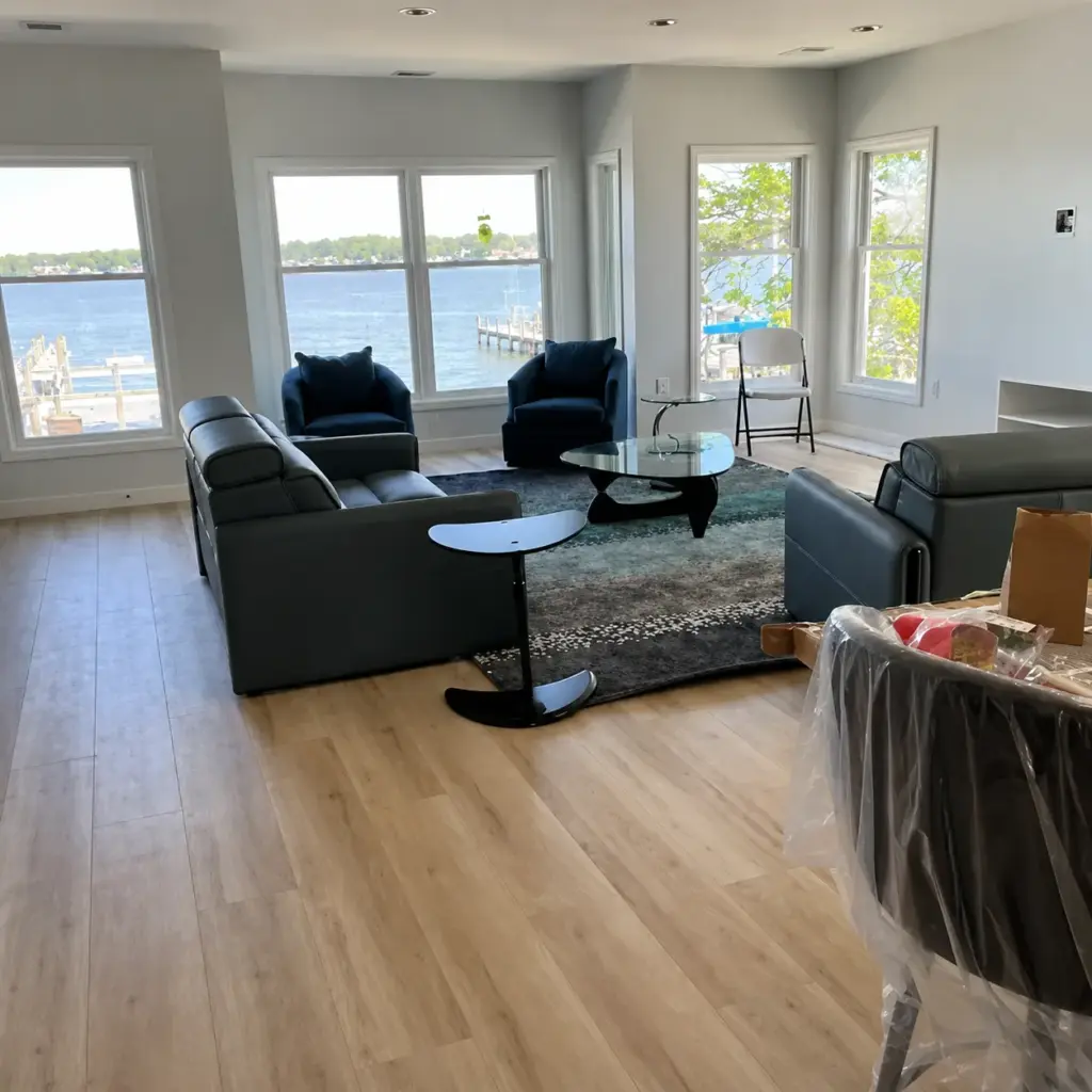 Lake Macatawa waterfront living room with large windows, lake views, modern seating, light wood flooring, and contemporary interior finishes.