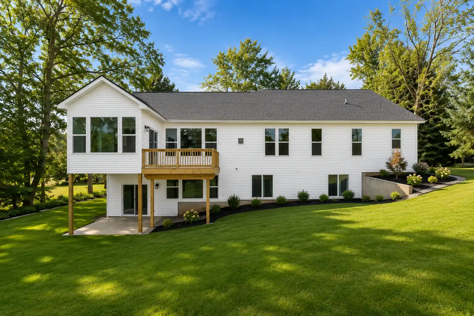Rear view of a completed custom home with a wooden deck on a landscaped lot in Michigan