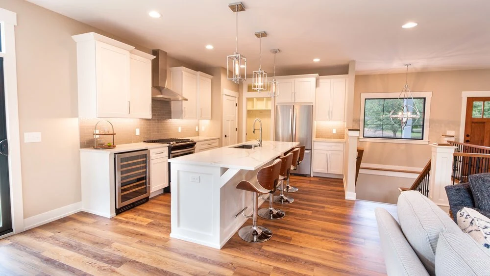 Modern custom home kitchen with white cabinets, a large island, pendant lighting, and wood flooring