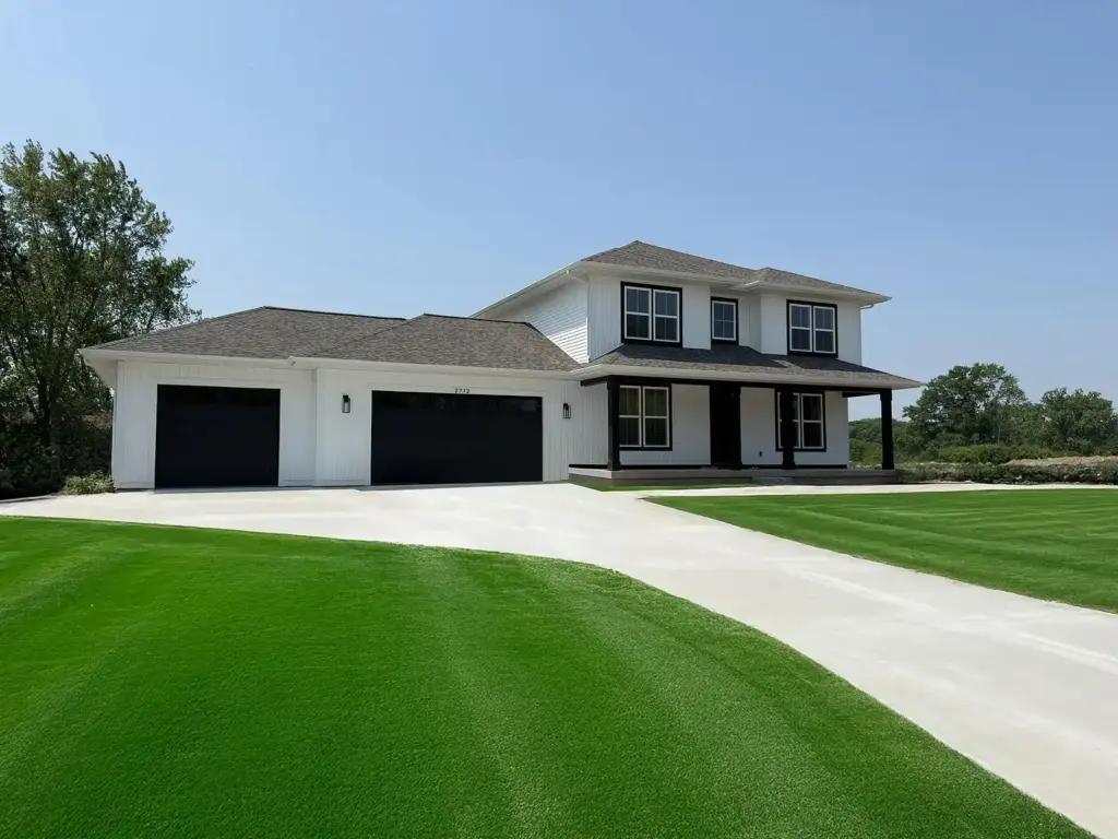 White modern farmhouse with black trim, three-car garage, and curved driveway