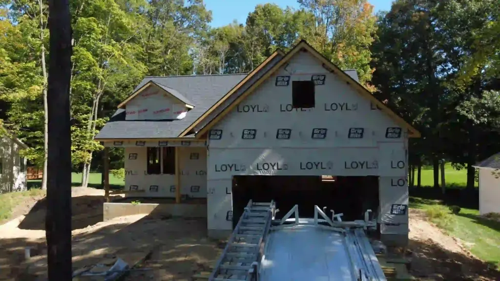 LOYL custom home under construction with roof shingles, exterior house wrap, and an unfinished garage