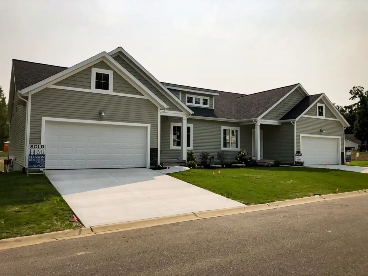 Gray custom home with white trim, multiple gables, two attached garages, and a landscaped front lawn