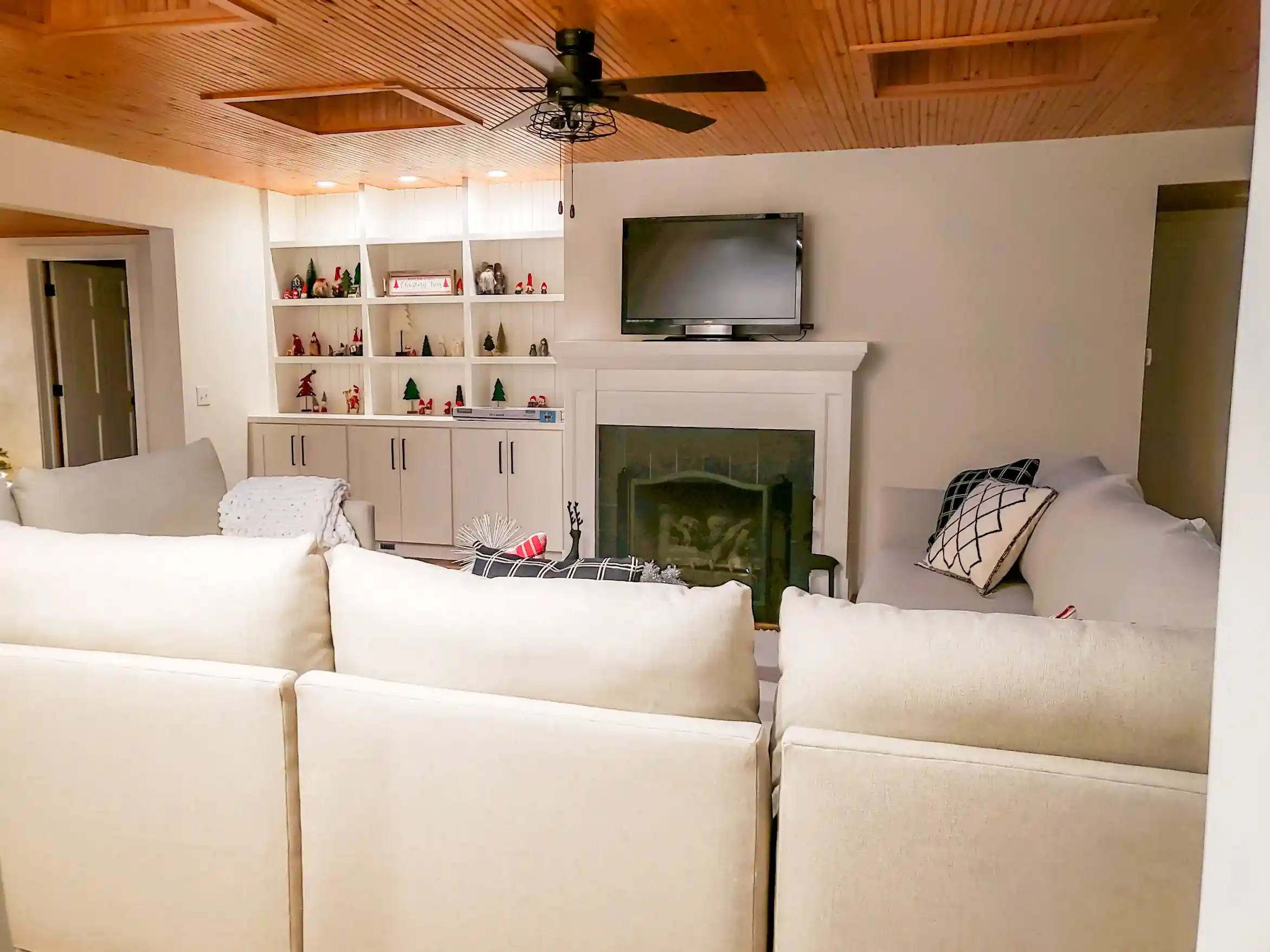 Cozy custom living room with wood ceiling, fireplace, built-in shelving, ceiling fan, and white sectional seating