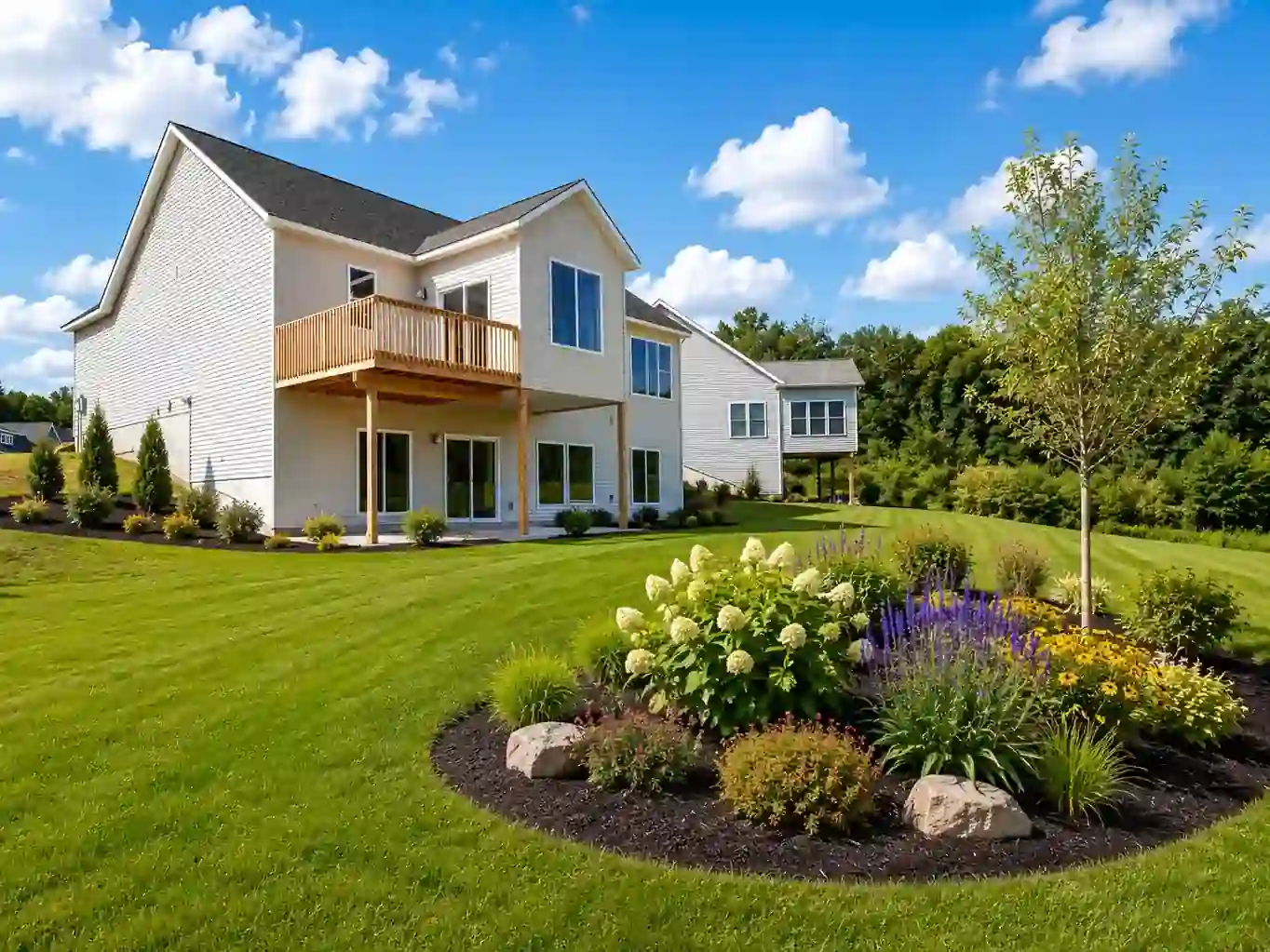 Rear exterior of a custom home with a raised wood deck, landscaped lawn, and colorful garden in West Michigan