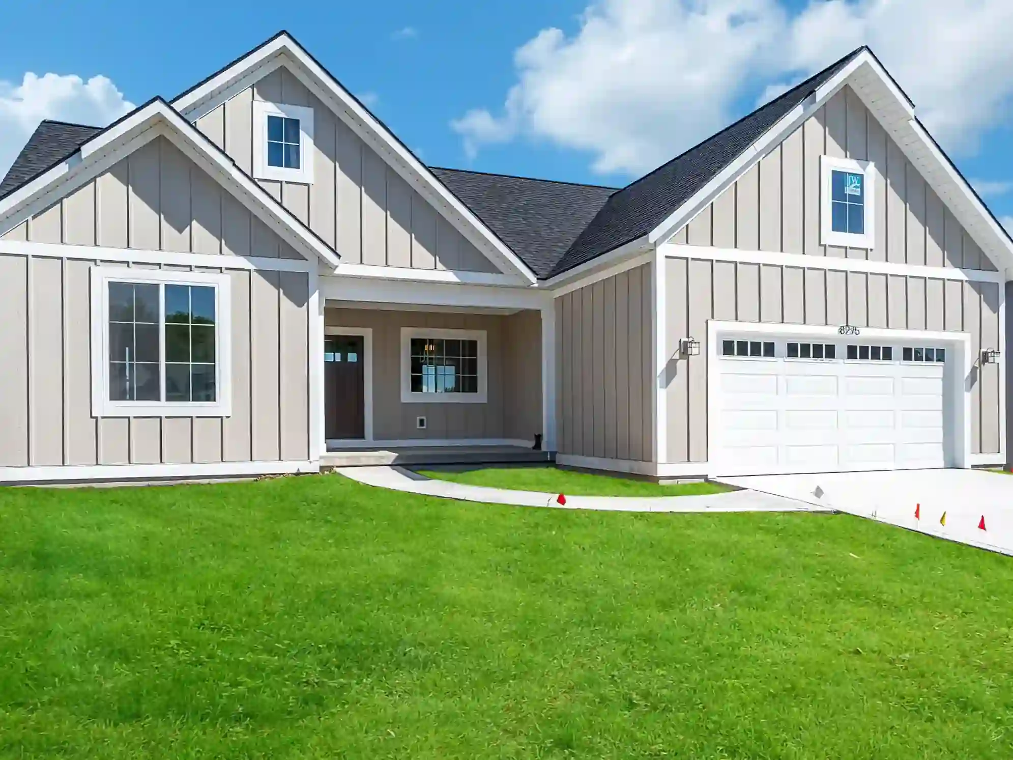 Gray board-and-batten custom home with white trim, attached garage, covered entry, and green lawn