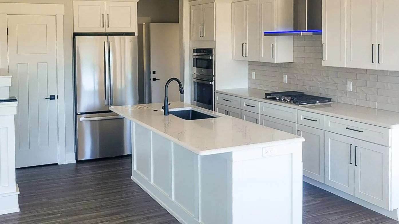 Modern white kitchen with quartz island, black faucet, stainless steel appliances, and subway tile backsplash
