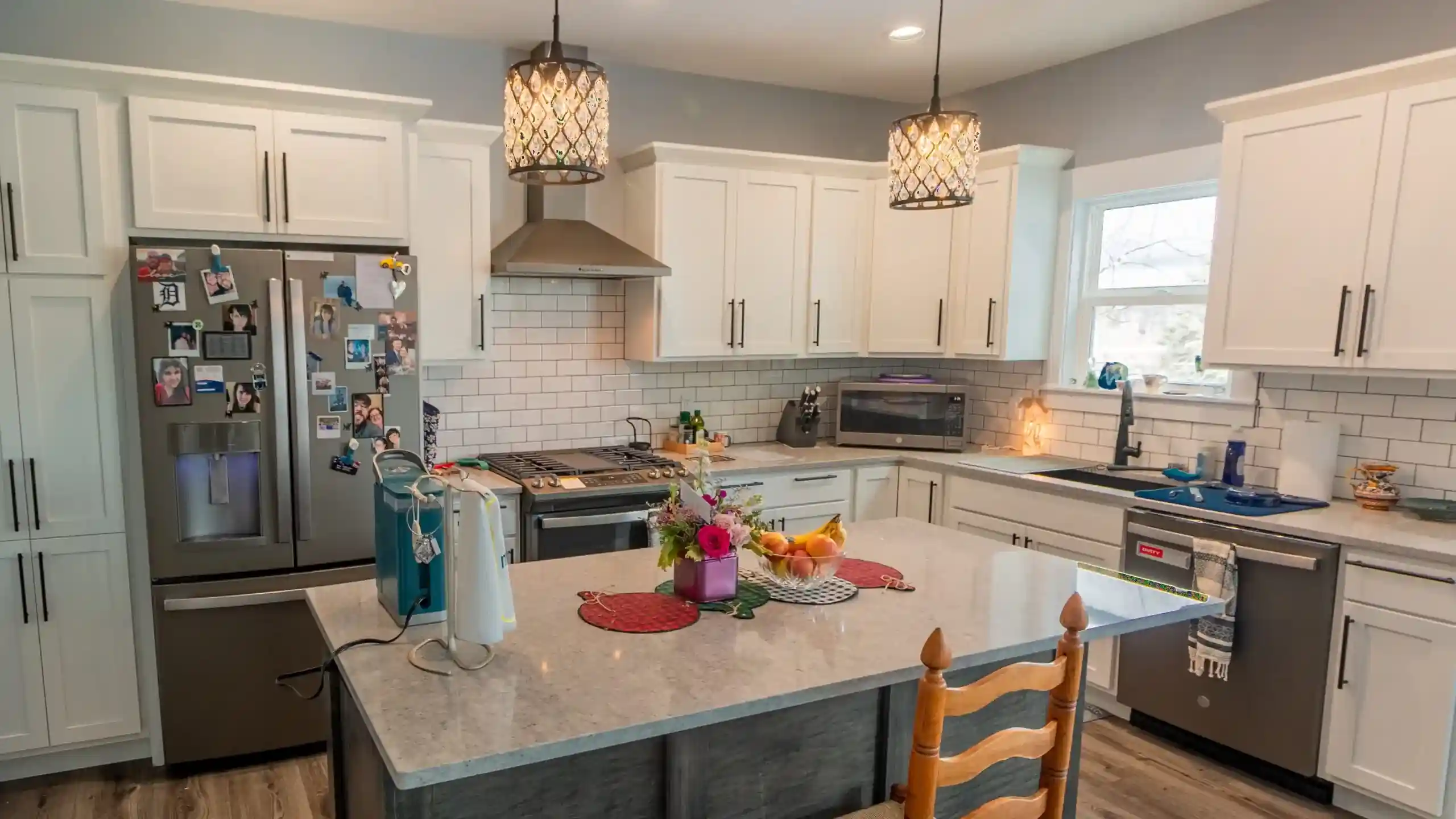 White custom kitchen with large island, pendant lights, and stainless steel appliances.