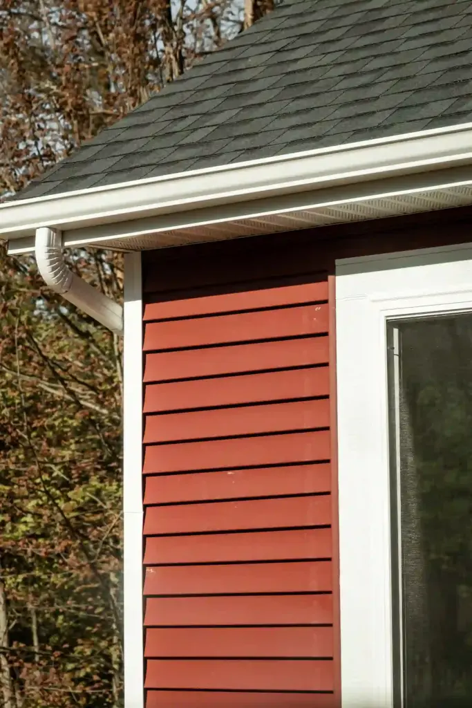 Red exterior siding with white trim, roof shingles, soffit, and gutter
