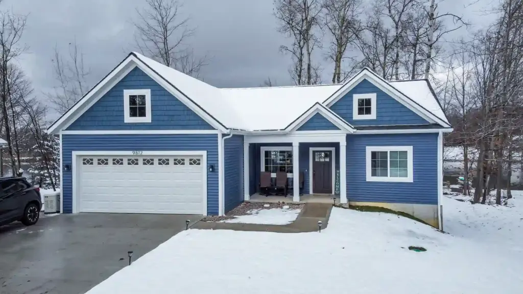 Blue custom home with white trim, attached garage, and snow-covered front yard