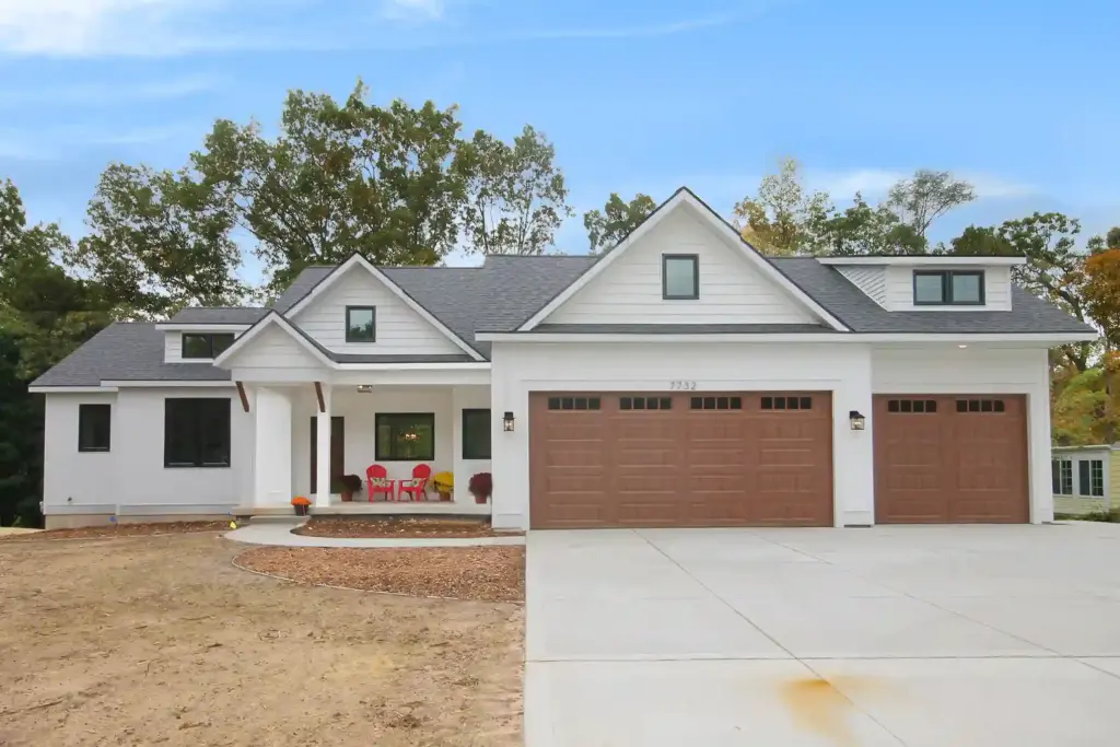 White custom home with wood-look garage doors, covered porch, and three-car garage