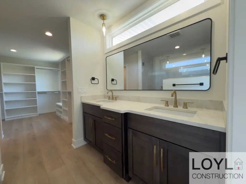 Custom home primary bath with double vanity, dark cabinets, and brass fixtures