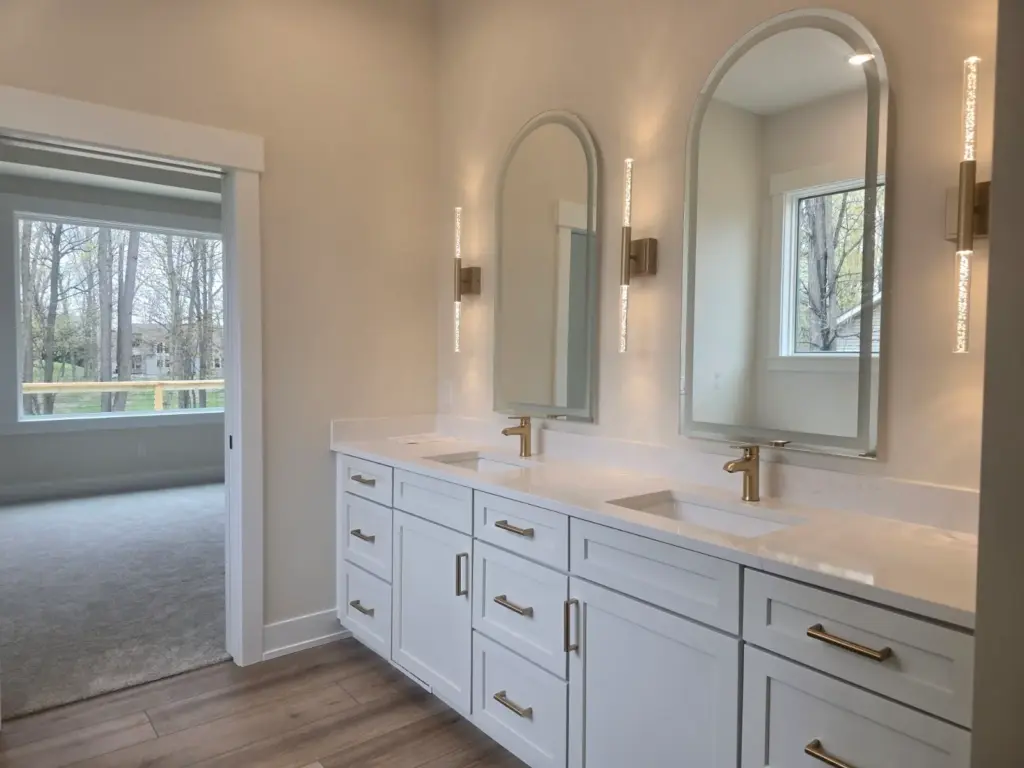 Custom home bathroom with white double vanity, arched mirrors, and brass fixtures