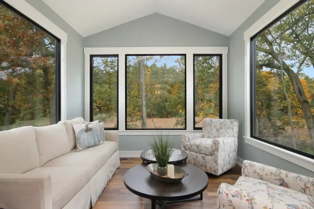 Custom home sunroom with black-framed windows overlooking autumn woods