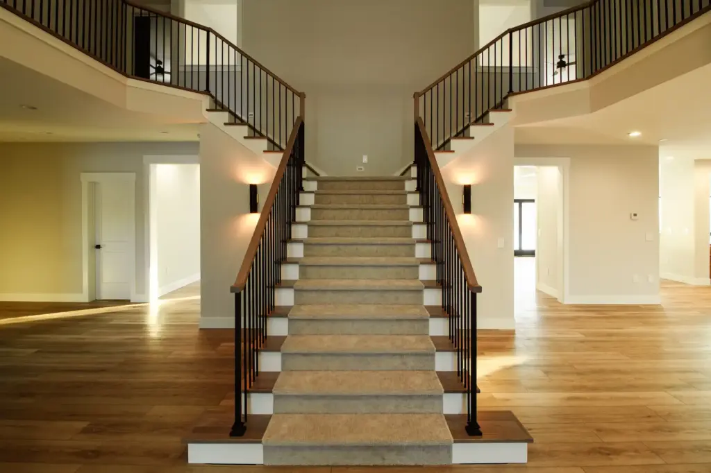 Grand staircase with black railings, wood handrails, and warm flooring in a renovated home