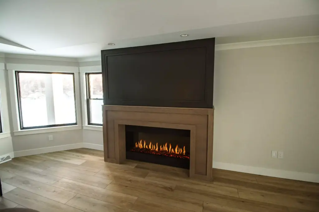 Modern fireplace with wood surround and dark paneled wall in renovated living room
