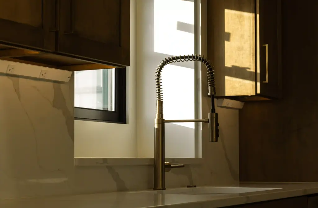 Brass spring kitchen faucet with stone backsplash and dark wood cabinets
