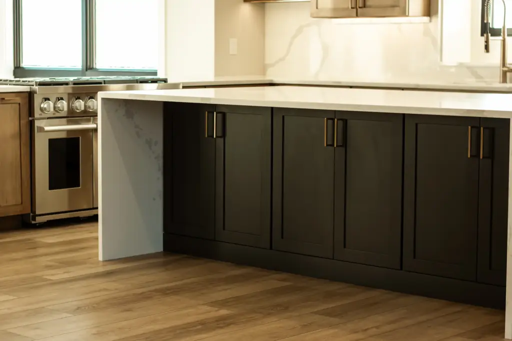 Dark kitchen island cabinets with brass pulls and waterfall stone countertop