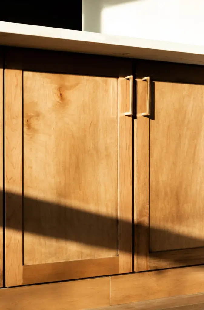 Sunlit wood kitchen cabinets with modern brass pulls and white countertop