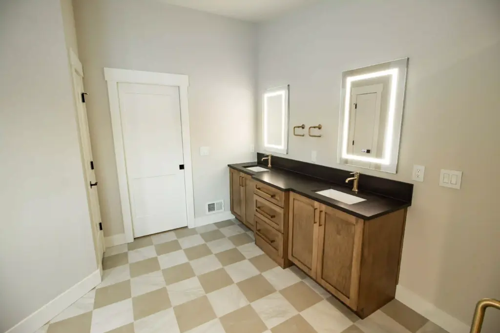 Renovated double vanity with wood cabinets, brass faucets, and lighted mirrors