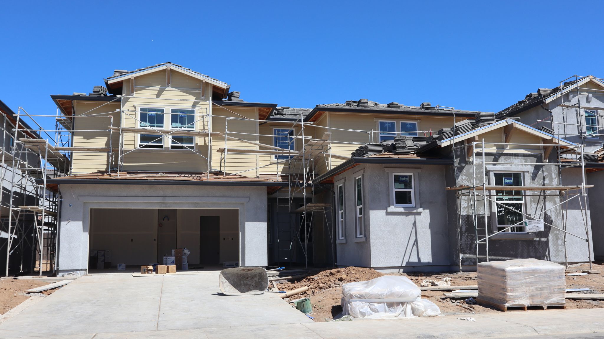 A large, modern house under construction with scaffolding against a clear blue sky.