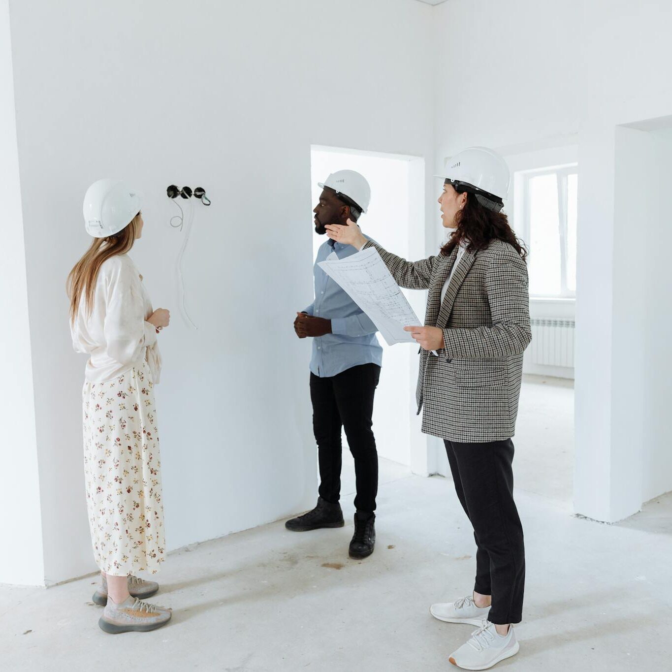 Three professionals discuss design plans inside a new house wearing hard hats.